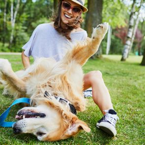 Joyful young woman playing with her dog outdoors in the park
