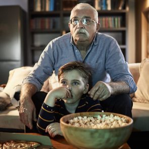 Grandfather and grandson watching a scary movie for Halloween with popcorn