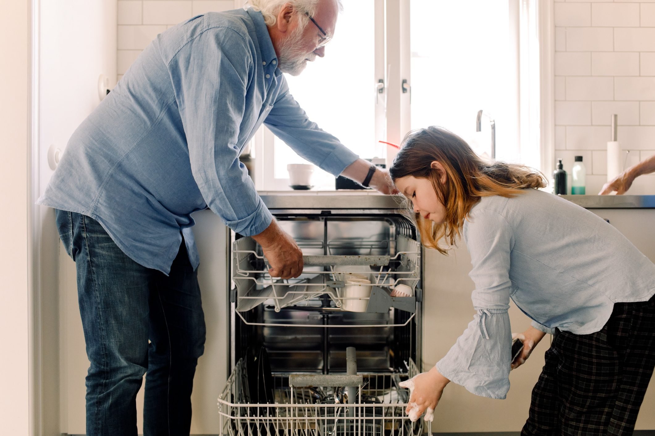 Grandfather assisting granddaughter in cleaning dishwasher at kitchen