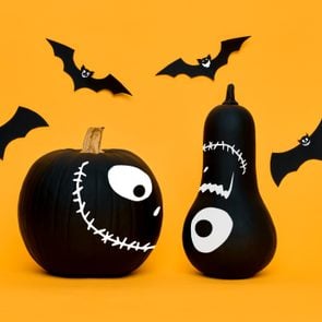 Cute Halloween pumpkins with funny smiling faces and paper bats flying over orange background. Halloween concept.