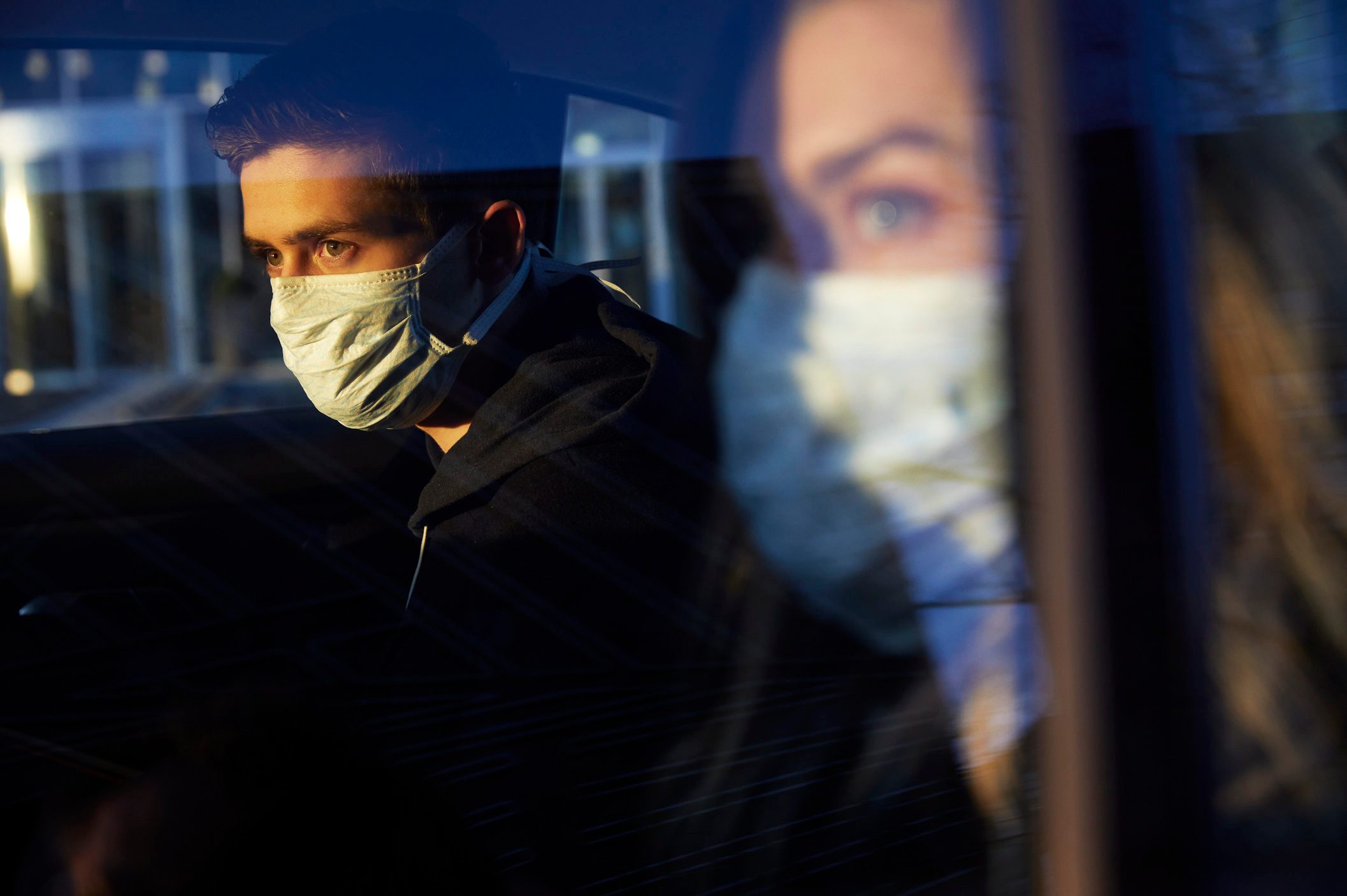 Young man and woman in car wearing a virus protective face masks