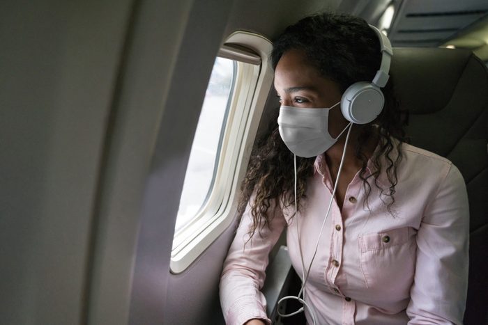 Woman listening to music while flying on an airplane wearing a facemask