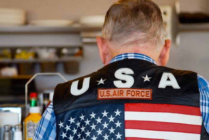 A man seated at a diner counter wearing an air force vest with a large american flag on the back.