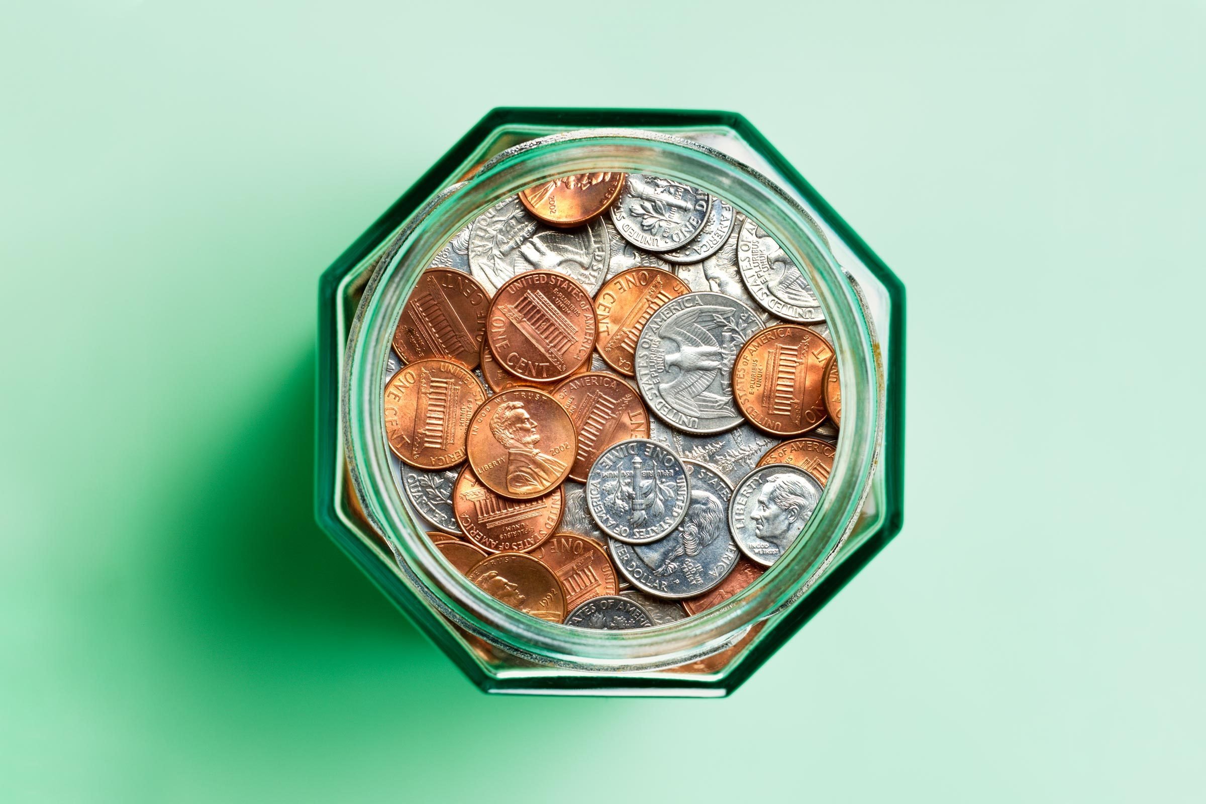 overhead view of coins in a glass jar. green background