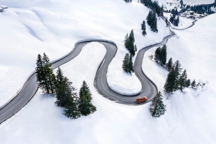 Aerial view of a red car driving in a snowy wilderness landscape