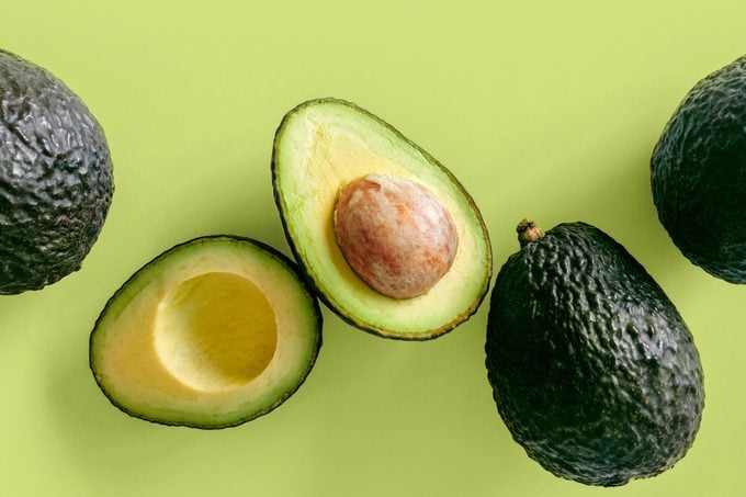 three whole avocados, one cut in half, on a green background