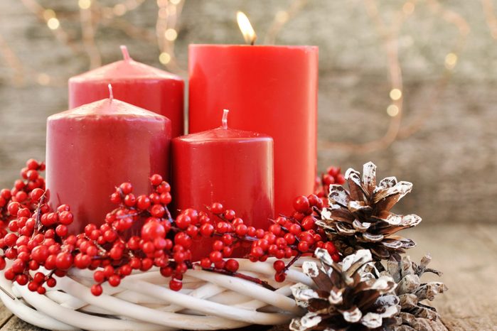 Four candles in a white wreath with red berries on a wooden rustic background with lights. advent calendar for Christmas.