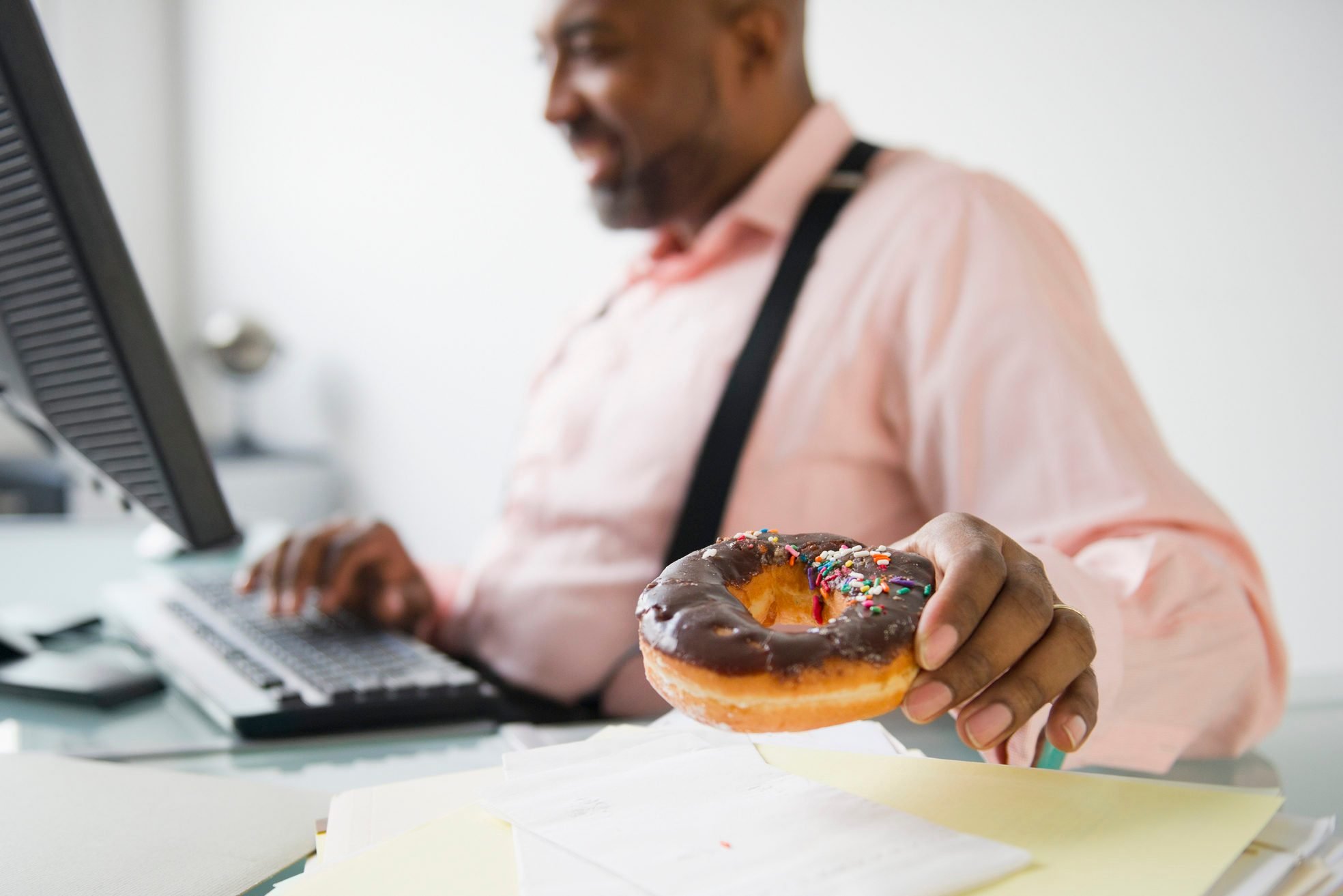 African American businessman eating donut at desk