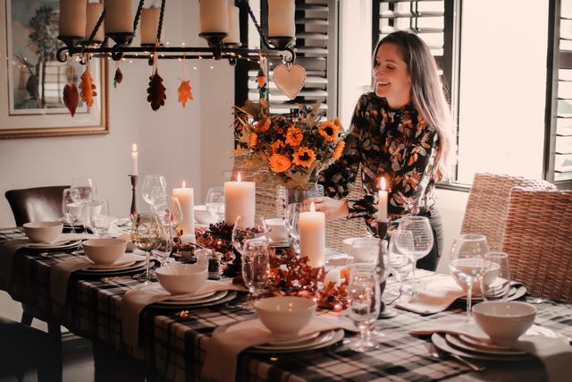 young woman setting the thanksgiving table with sunflowers and autumn decorations