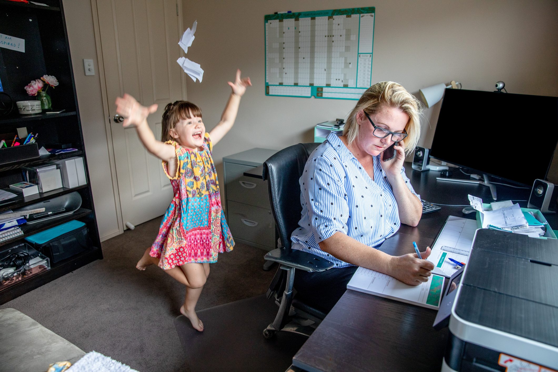 Middle Aged Women working from home in office whilst also looking after her young daugther.