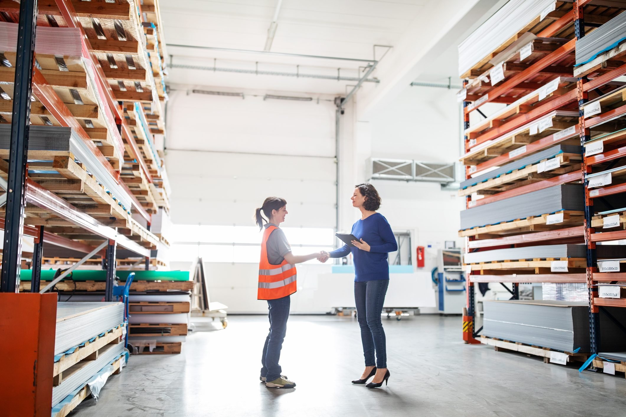 Businesswoman shaking hands with worker in large warehouse. Manager and worker handshake in storehouse