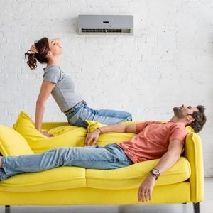 young man and woman resting on yellow sofa under air conditioner at home