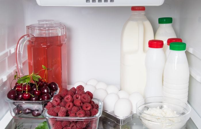 on a shelf in a white refrigerator, products of animal and vegetable origin, cream, milk, kefir, eggs, cottage cheese, compote in a jug and fresh berries