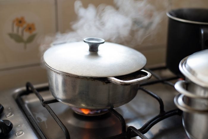 Close-Up Of Cooking Pot With Steam On Stove Top At Home