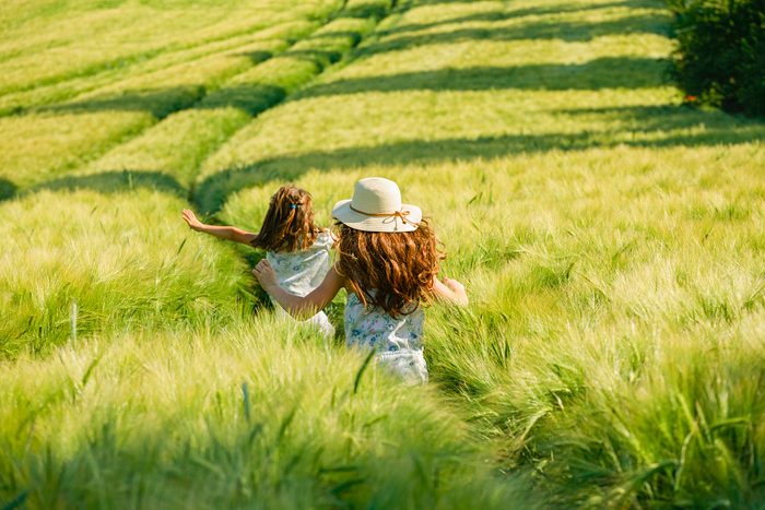 Playful, carefree girls running in sunny, idyllic rural green wheat field