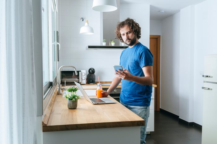 Man with smartphone and laptop in the kitchen
