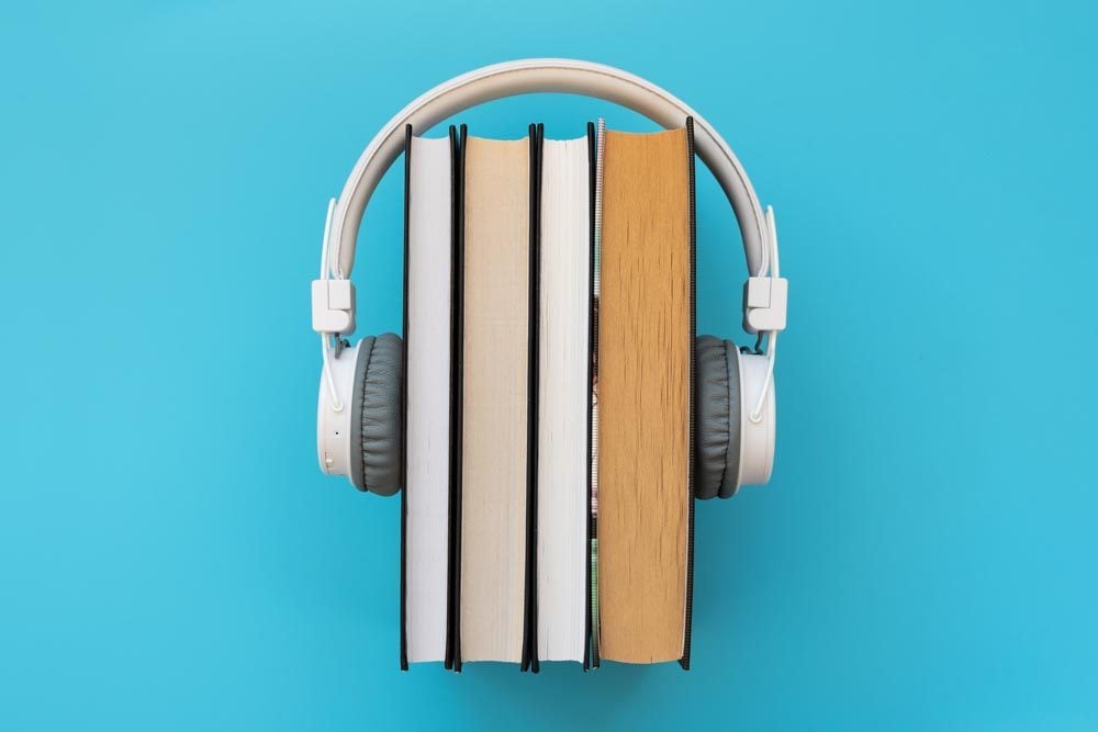 White headphones with stack of books on blue background. Audio books or modern education concept