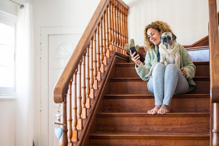 Woman sitting on stairs, using smartphone with pug on her lap