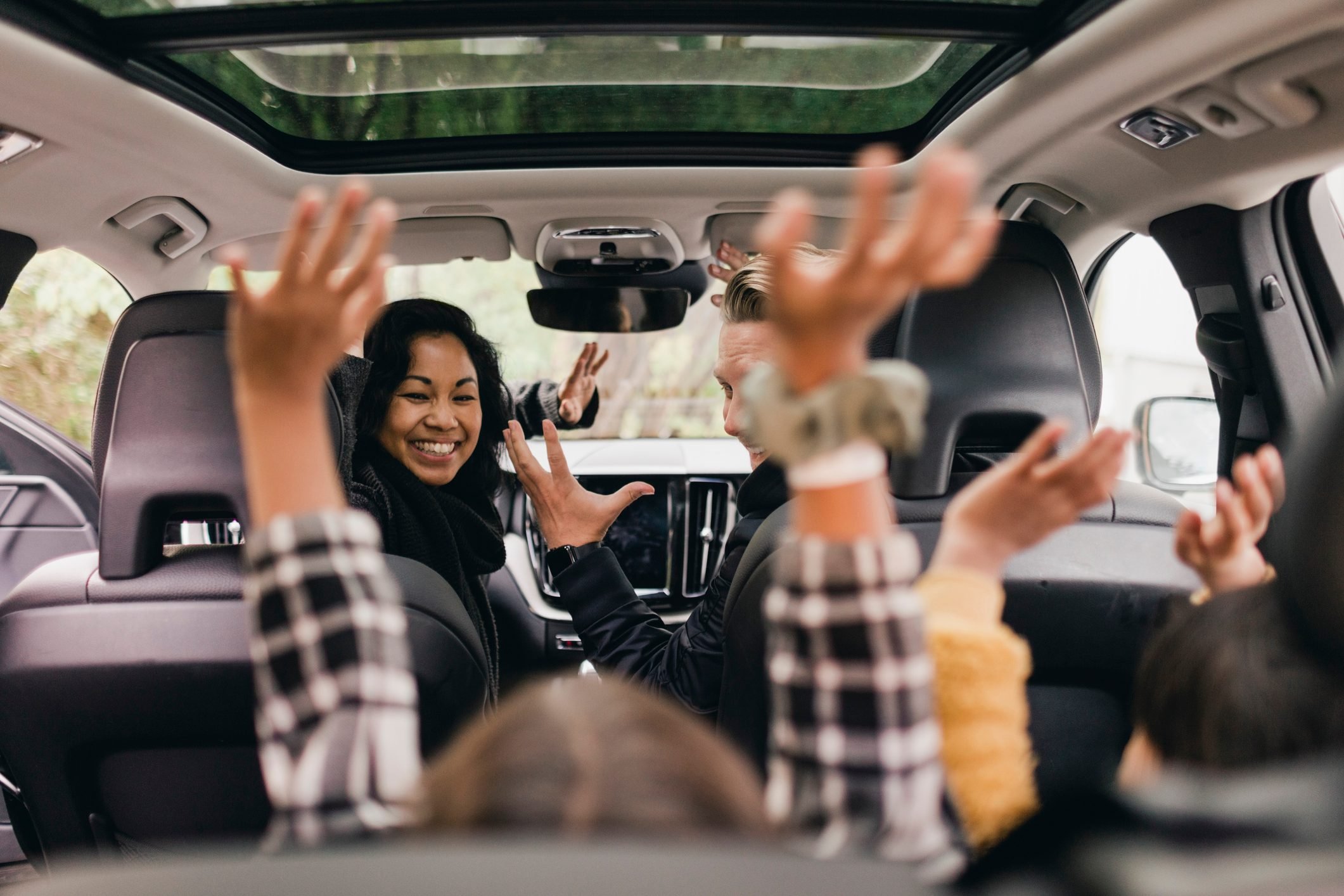 Familia alegre levantando la mano mientras disfruta de un paseo en auto eléctrico