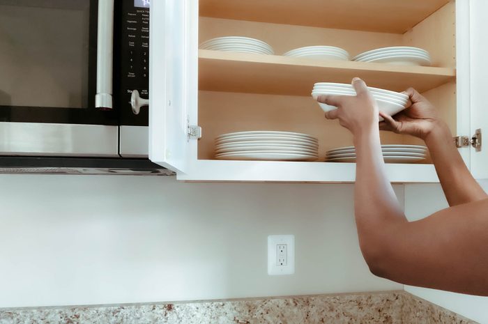 Woman Puts Dishes Into Kitchen Cabinet