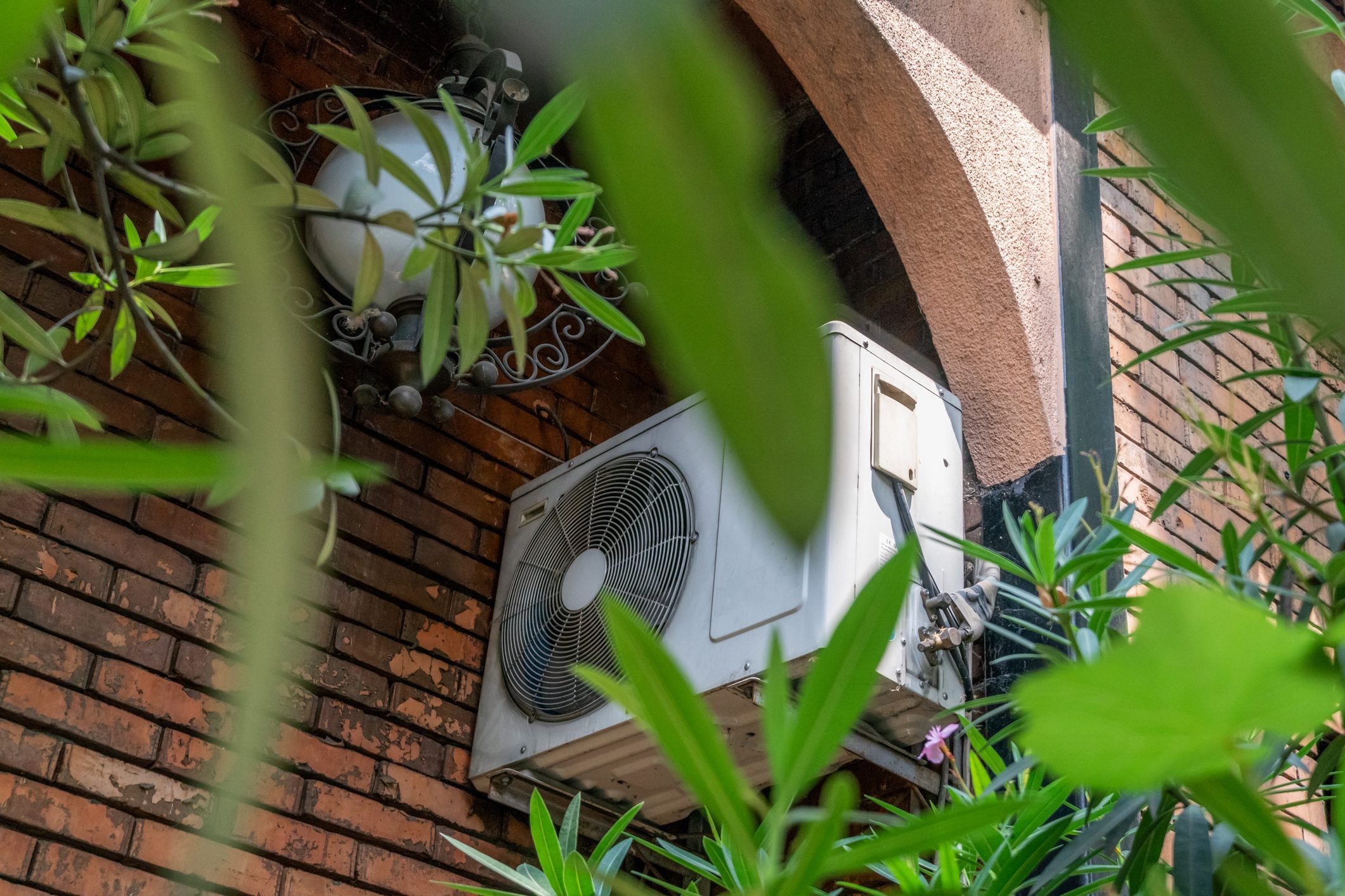 White air conditioner on a brick wall of a building outside among the leaves of trees