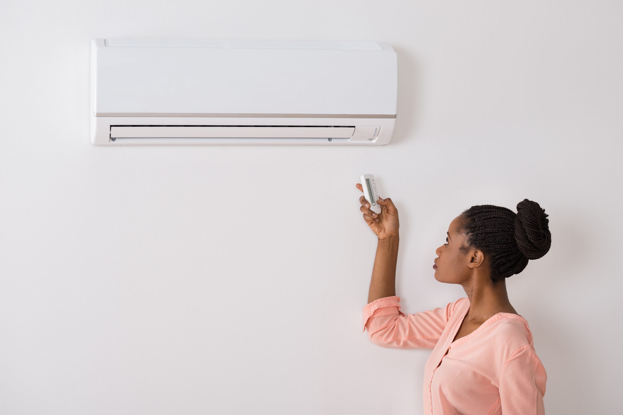 Woman Operating Air Conditioner With Remote Control