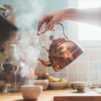 Arm of man pouring boiling water into bowl in kitchen