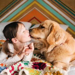 Girl lying on a bed kissing her golden retriever dog