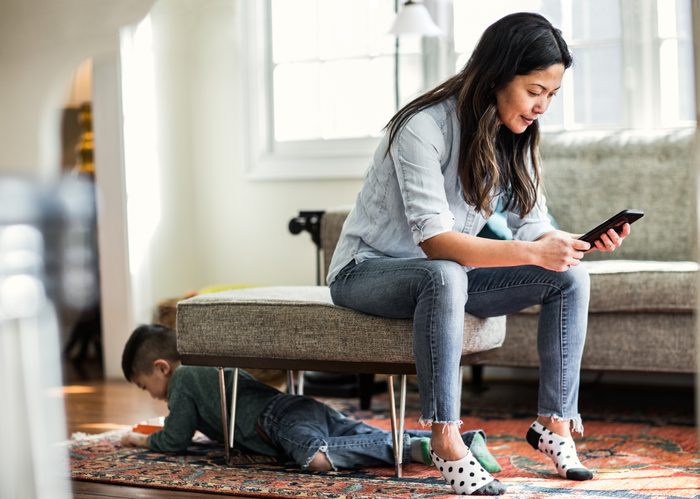 Woman using smartphone at home with child in background