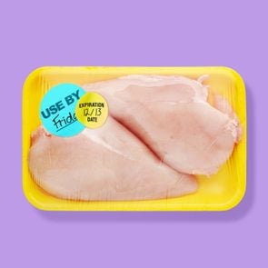 purple background with raw chicken in a yellow Styrofoam tray with two different expiration and Best Buy stickers.