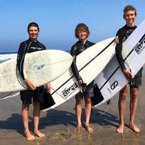 Spenvser Stratton, Taj Ortiz-Beck, and Adrian York on the beach holding surf boards