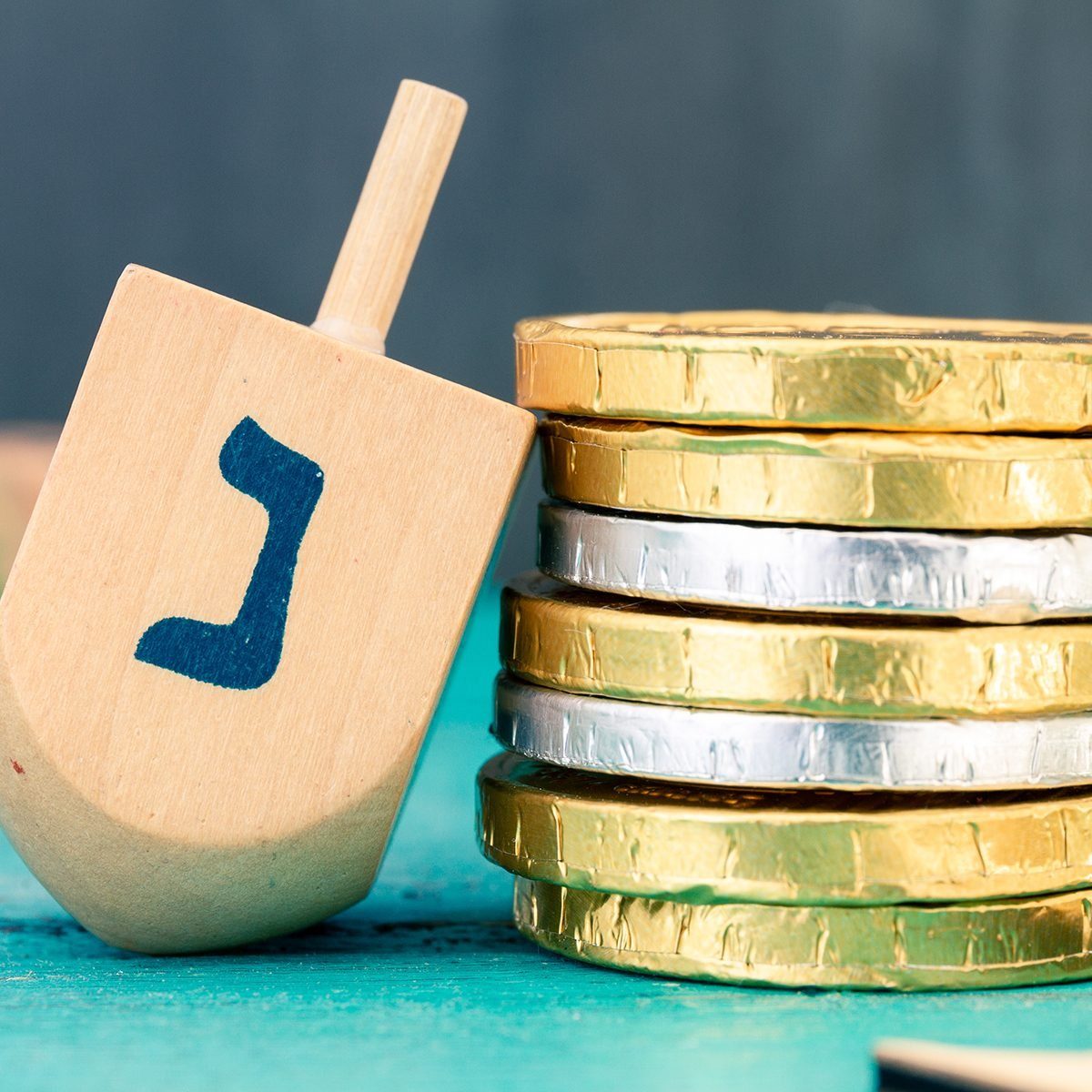Hanukkah dreidels with some Hanukkah coins and Hanukkah candles on a vintage wood green background. Translation of the hebrew text: Letter N