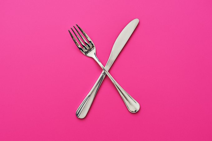 Tenedor y cuchillo cruzados, aislado sobre fondo de color rosa