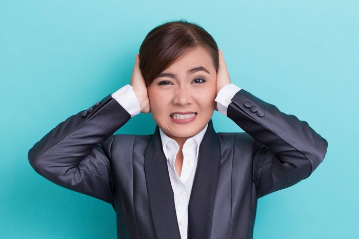 Businesswoman Covering Ears While Standing Against Blue Background