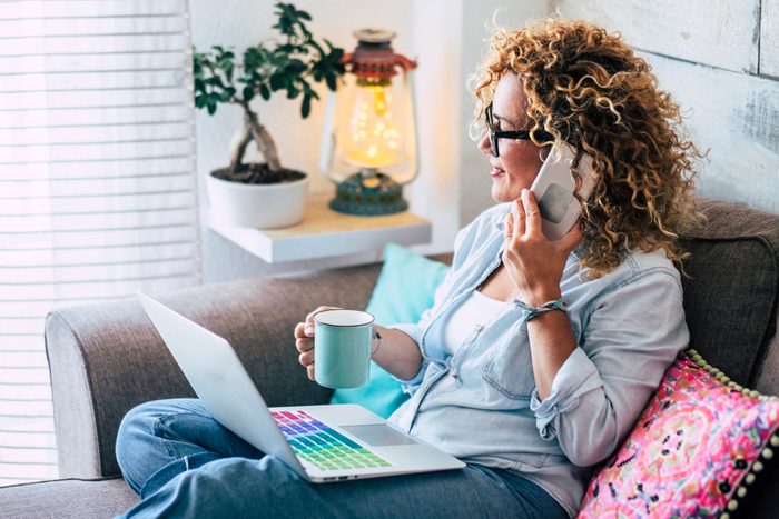 Woman on couch at home with coffee mug, laptop and cell phone