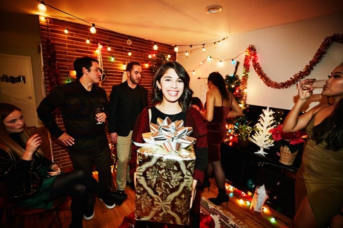 Smiling woman holding present during holiday party with friends in home