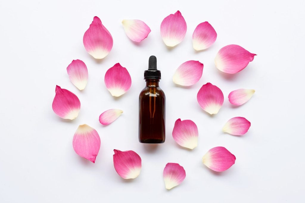 Bottle By Rose Petals Against White Background