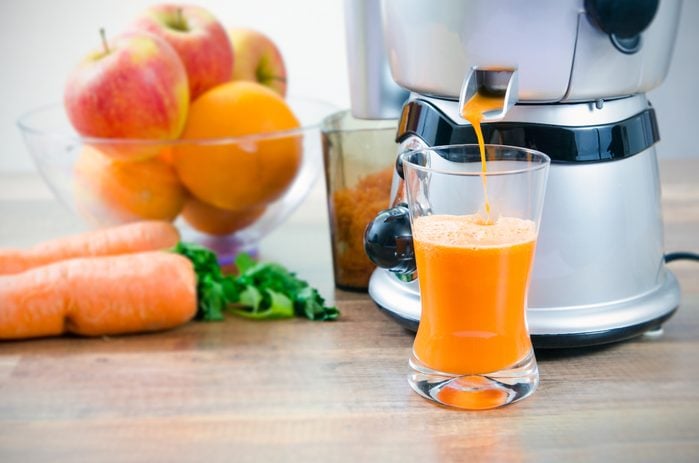 Juicer and carrot juice. Fruits in background