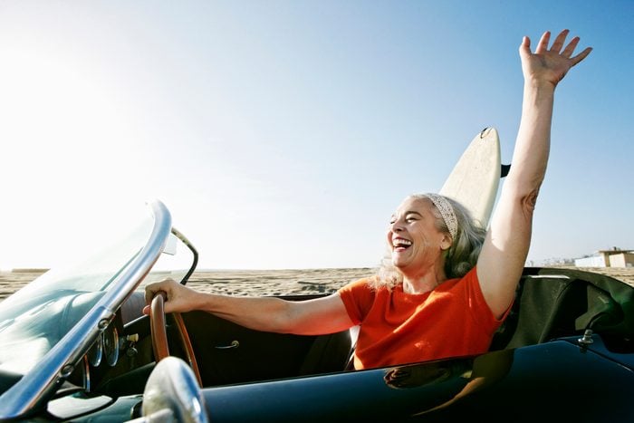 Older Caucasian woman in convertible car with surfboard on beach