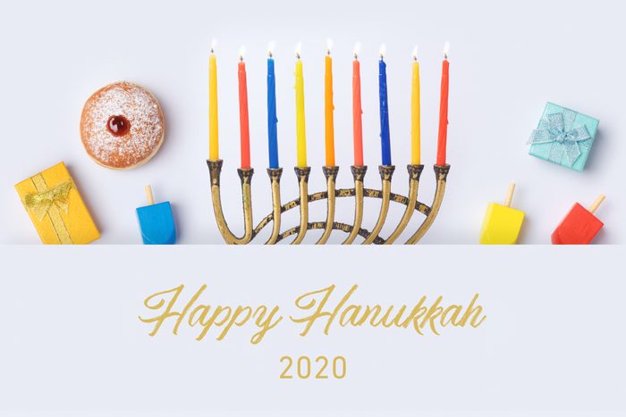 Jewish holiday Hanukkah flat lay design with menorah, sufganiyot, dreidels, and gifts on white background. Top view from above with text: "Happy Hanukkah 2020"