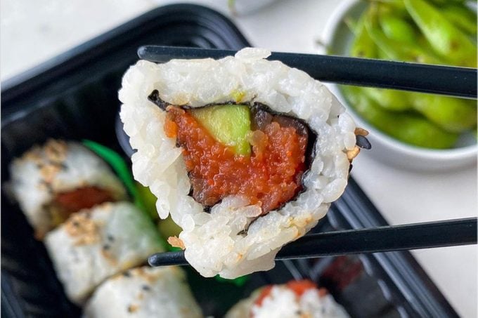 chopsticks holding a piece of a spicy tuna sushi roll