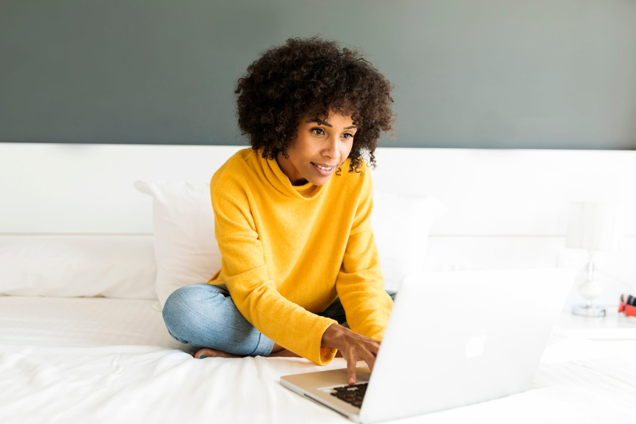 Smiling woman sitting on bed using laptop