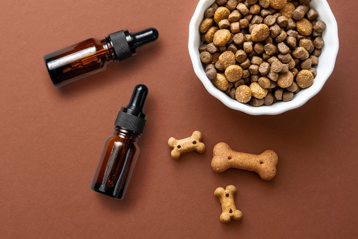 overhead view of two cbd glass vials next to a dog food dish and bone shaped treats on a brown background