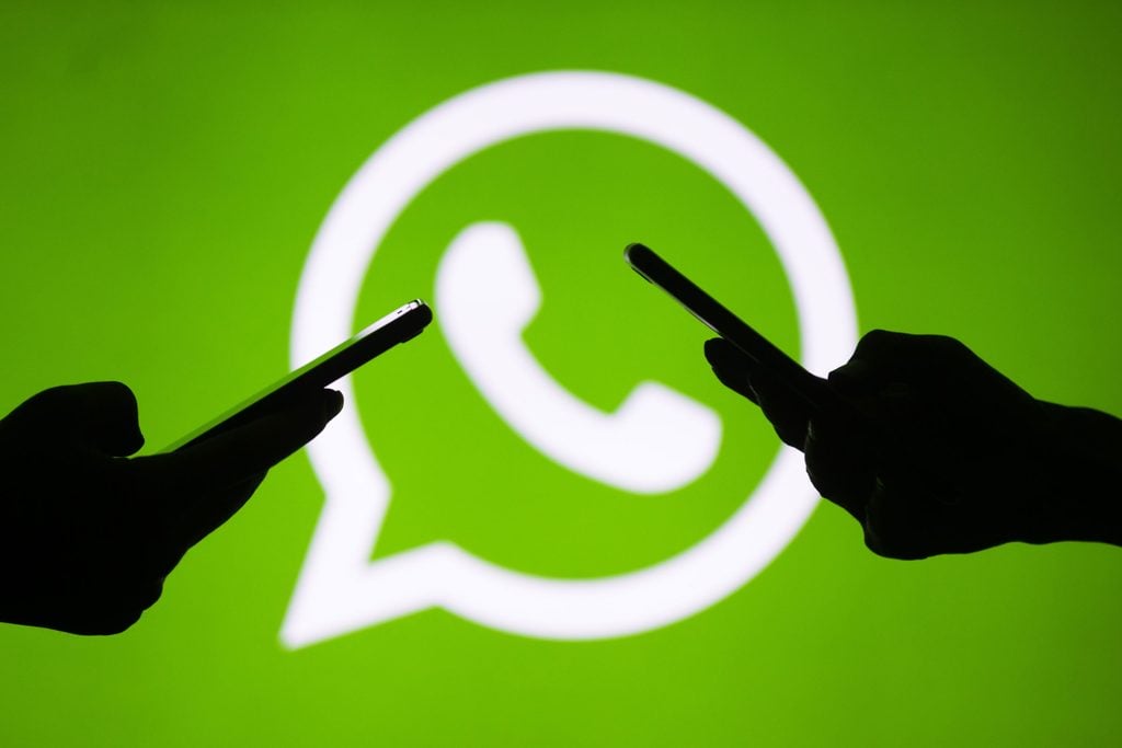silhouettes of hands holding phones using WhatsApp with the whatsapp logo in the background