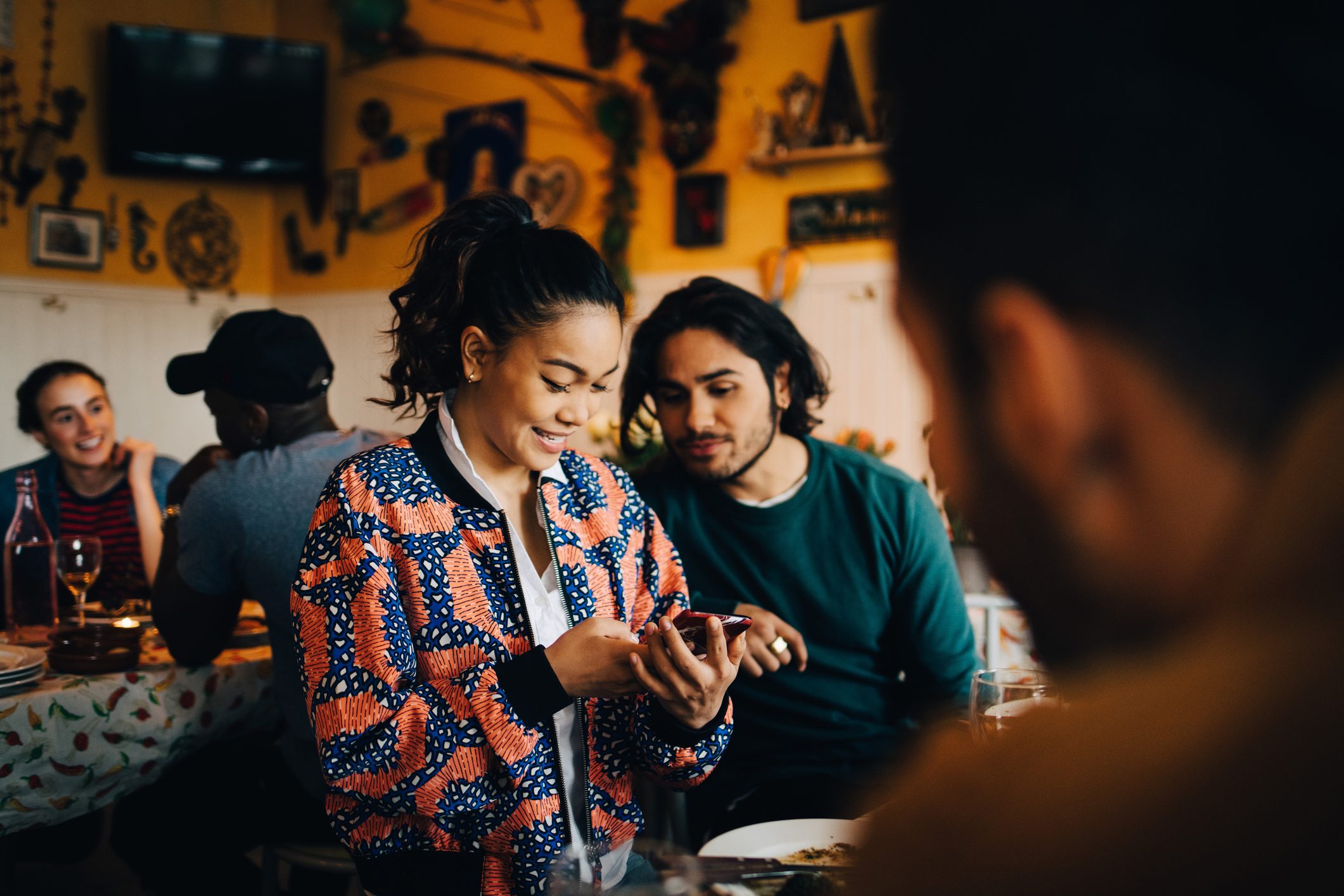 Smiling young woman sharing smart phone with male friend while sitting at restaurant during dinner party