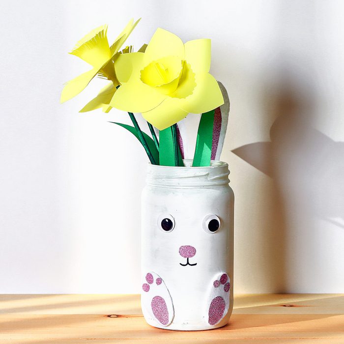 DIY Easter vase bunny with narcissus, daffodils from glass jar, felt, eyes on white wall background