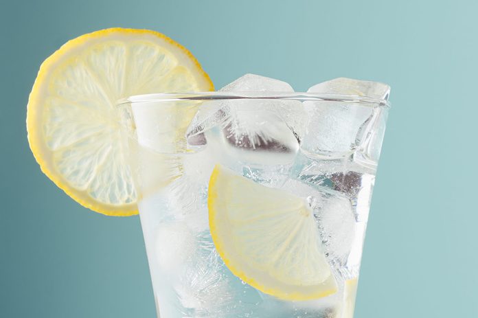 Healthy fresh tonic with lemon, ice cubes, soda in misted glass on pastel green color background, closeup, half, details, top.