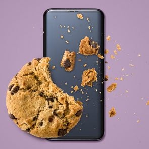 a chocolate chip cookie with crumbs on top of a smartphone on a purple background
