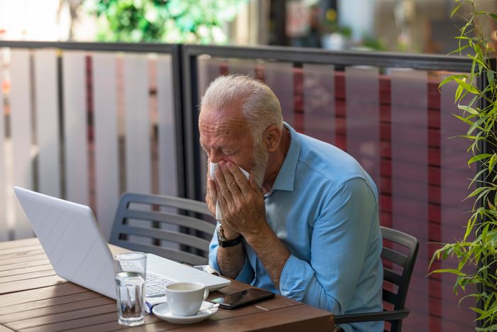 Older Man is Blowing Nose in Paper Tissues in Restaurant Garden