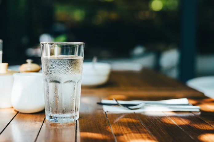 A glass of water served on table in an outdoor restaurant against beautiful sunlight
